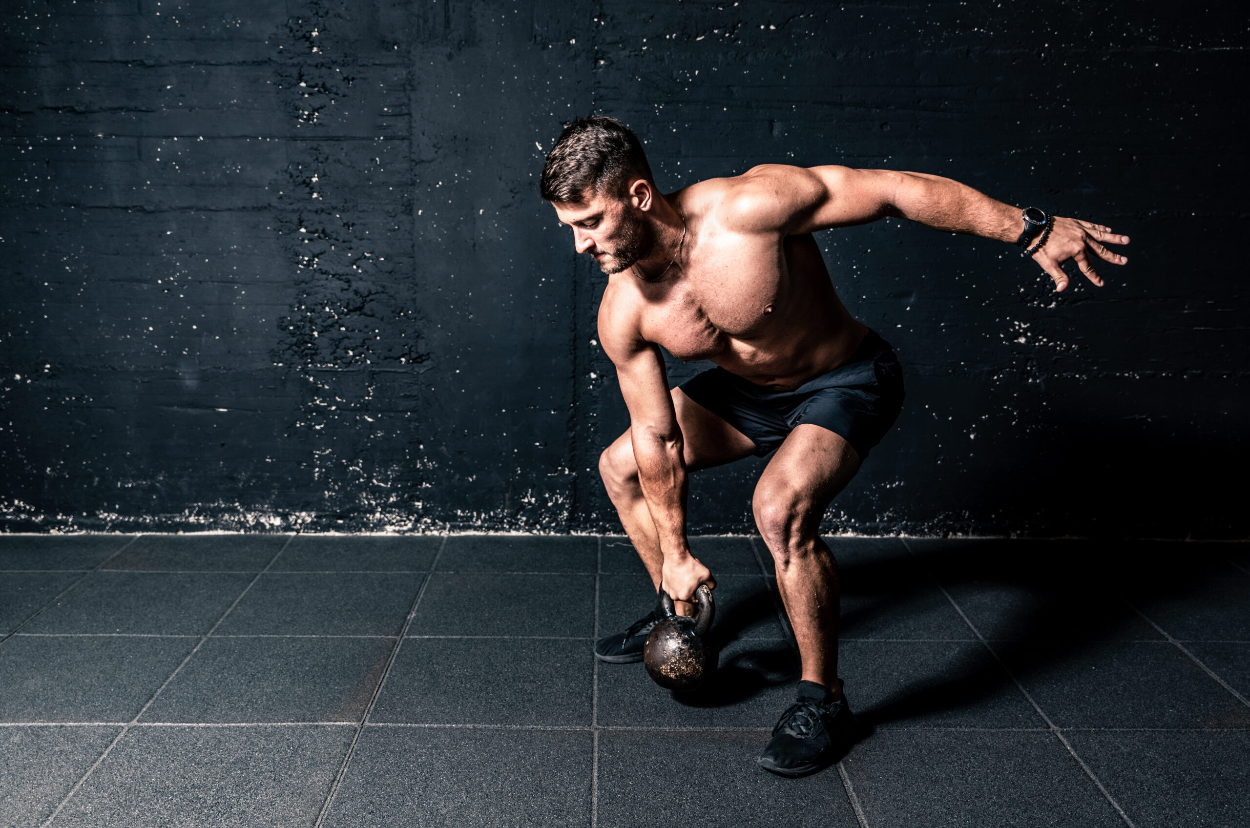 Young strong sweaty focused fit muscular man with big muscles holding heavy kettle bell for training hard core workout in the gym real people