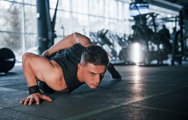 Strong young man in sportive clothes doing push ups in gym